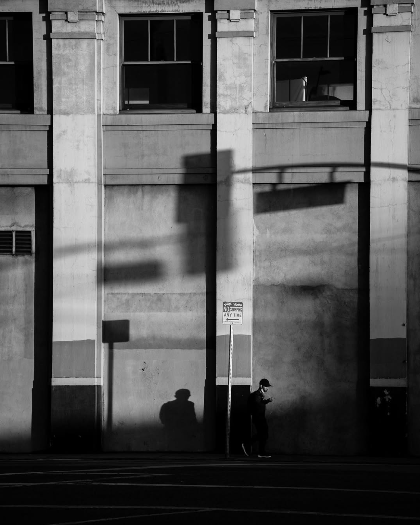 A pedestrian walks past a sunlit building facade with long dramatic shadows